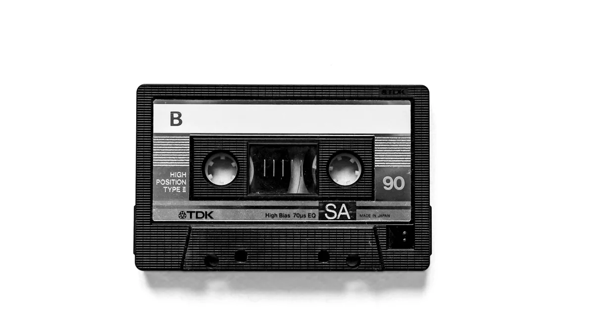 A cassette tape photographed on a light background in black and white.